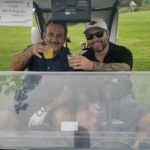 Two golfers in their cart with drinks.