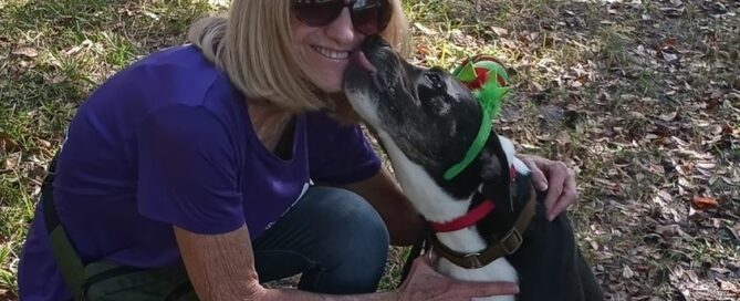 Kelly, wearing holiday head gear, sitting on the ground giving Joan a kiss.