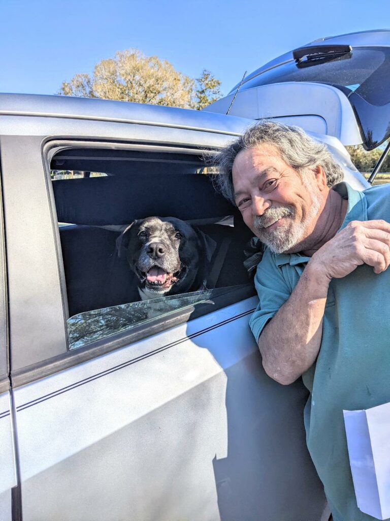 Bonny sitting in the back seat of her adopter's car with Mark (adopter) leaning up against the window.