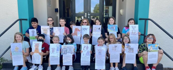 All the kids holding their pictures and stories on the school steps.