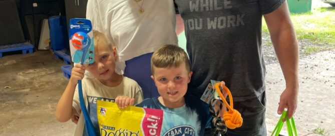 Colton holding a bag of treats with his family holding other donations.