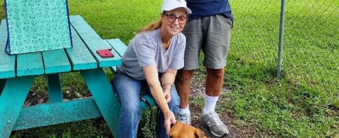 Duey in the yard at Satchel's sitting at the feet of his new mom also seated, dad by their side.