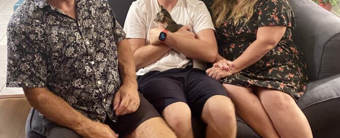 Lizzy on the lap of his new human sibling, mom and dad sitting beside on the couch