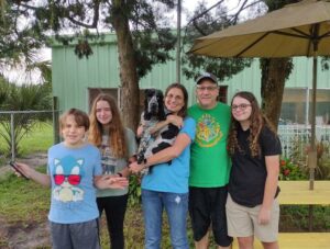 Arthur in the arms of one of his new siblings in the yard at Satchel's.. Mom and dad and other siblings by his side.