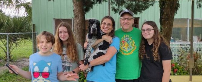 Arthur in the arms of one of his new siblings in the yard at Satchel's.. Mom and dad and other siblings by his side.