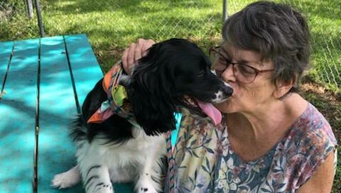 Belle's mom kissing Belle who is sitting on the picnic table in the yard at Satchel's.