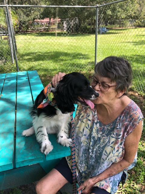 Belle's mom kissing Belle who is sitting on the picnic table in the yard at Satchel's.