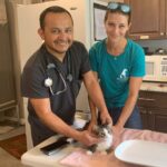 Dr. Wilson and Michal Anne holding a kitten on the table at Satchel's, preparing to give a rabies vaccine.