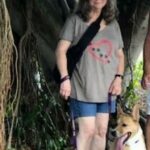 Quinton outside sitting beside his standing mom, both beside a tree.