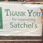 Tiki in the arms of her momma beside the "Thank you for Supporting Satchel's" sign at Satchel's Birthday Party.