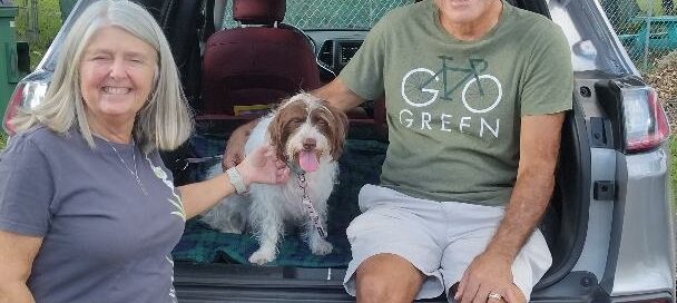 Nicki sitting in the back of an SUV, mom and dad by side petting her.