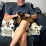 Princess on dad's lap with 2 canine siblings beside.