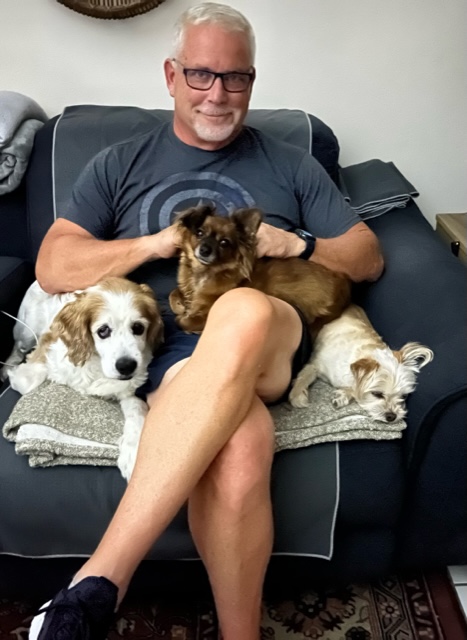 Princess on dad's lap with 2 canine siblings beside.