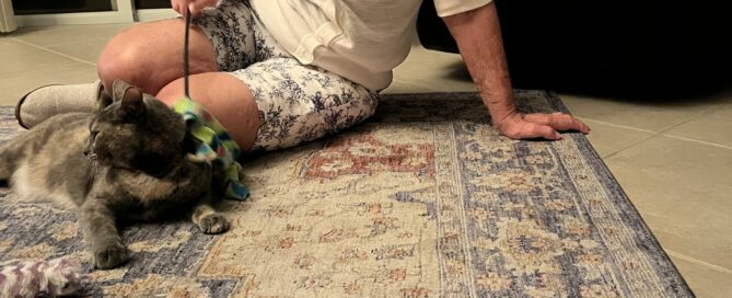 Muneca on the rug, mom sitting beside her stroking her with a feather.