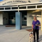 Gail with Bernie on leash standing outside Alta VIsta Elementary School.
